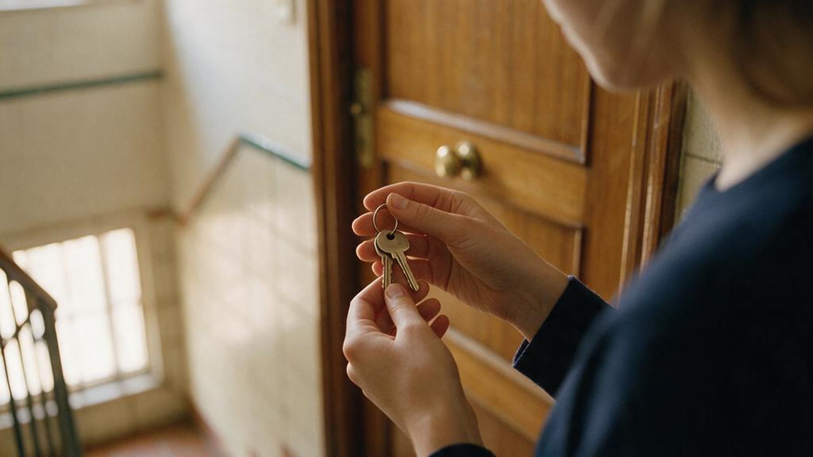 Manos sosteniendo las llaves de un apartamento frente a la puerta de un edificio español